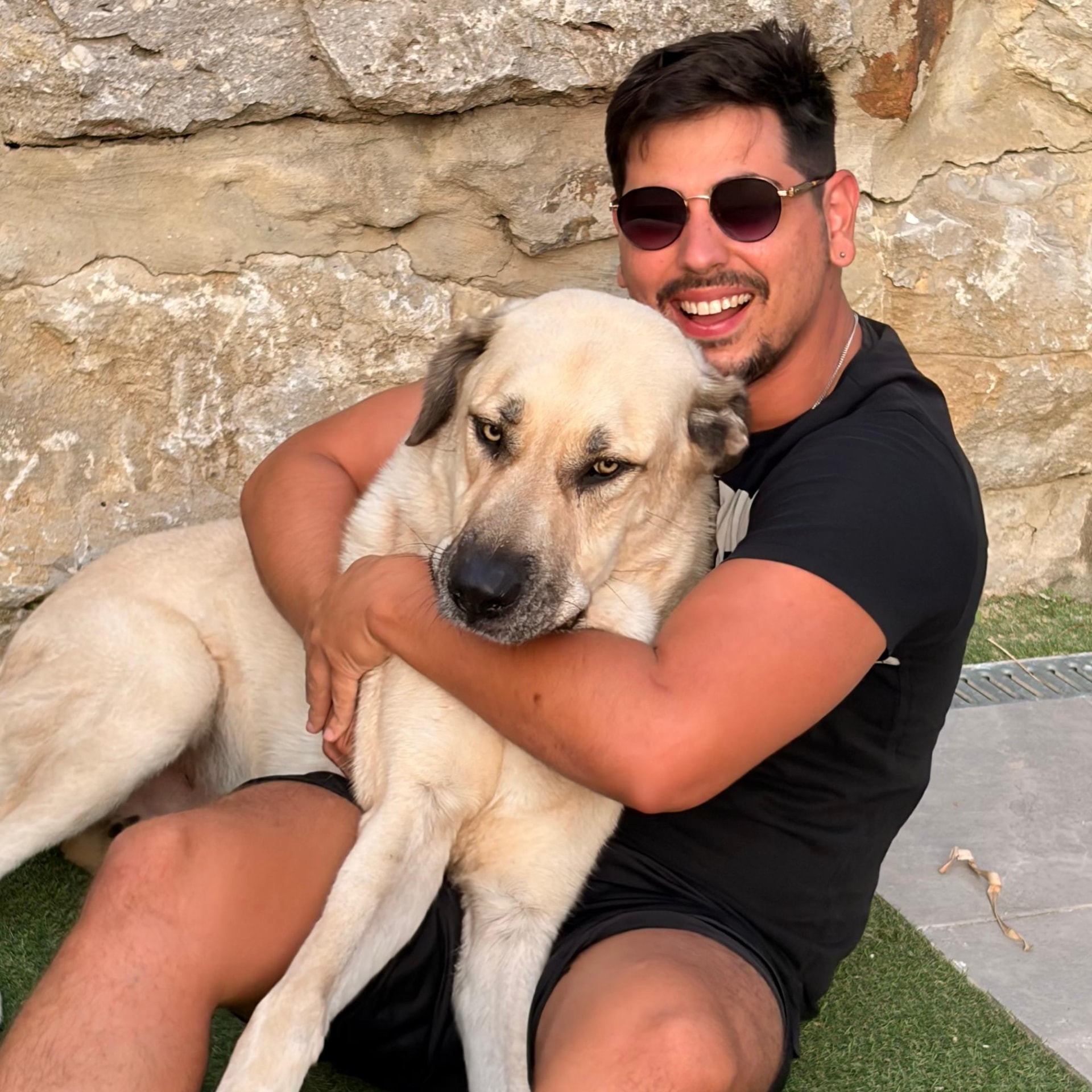 The owner of Happy Tails Cádiz smiling while hugging a large, happy tan dog